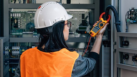 A person in a hard hat using a multimeter