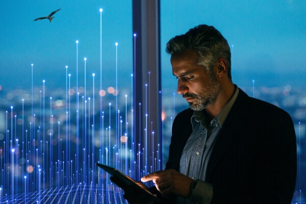 Man using a tablet near a window overlooking the city, overlaid with a graphic of transmission nodes
