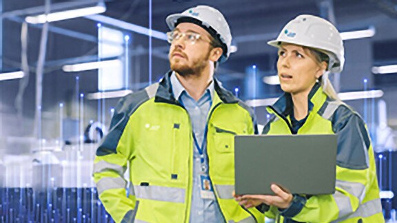 Técnicos da Johnson Controls utilizando notebook, sobreposto com um gráfico de nós de transmissão ao fundo