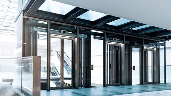 Um lobby bem iluminado em um edifício, com portas de vidro que levam a escadas rolantes